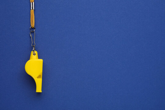 One yellow whistle with cord on blue background, top view. Space for text