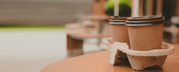 Takeaway paper coffee cups with plastic lids in cardboard holder on wooden table outdoors, space for text. Banner design