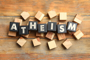 Word Atheism made of black cubes with letters on wooden table, flat lay