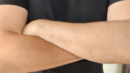 Close up of crossed arms of a young Mexican man, with a black shirt.