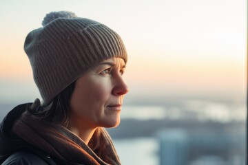 Young woman in a hat and scarf looking out the window at sunset