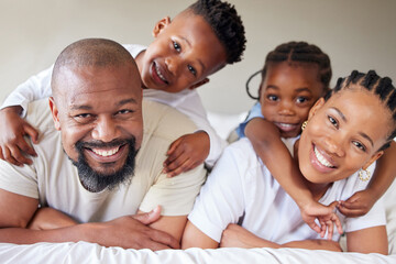 Portrait of a joyful african american family lying on each other on a bed in a bedroom. Black...