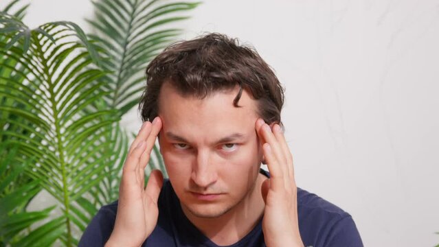 Portrait of a mysterious man looks attentively with a piercing gaze, massages his temples, grins, rubs his chin, tunes in to a hypnosis session. Alternative methods, bodily practices, stress relief
