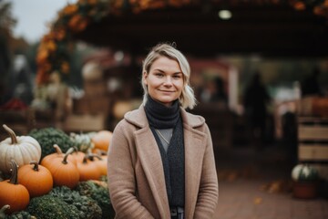 Beautiful blonde woman in a coat and scarf on a background of pumpkins.