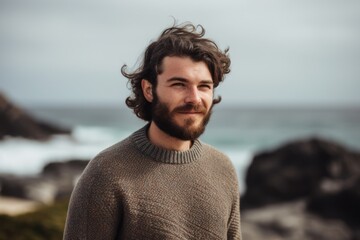 Fototapeta premium Portrait of handsome young man with long curly hair wearing warm sweater at the beach