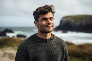 Portrait of a handsome young man smiling at the camera while standing on the beach by the sea