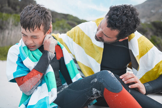 What is swimmers ear. Shot of a young boy experiencing discomfort in his ear while out surfing with his dad.