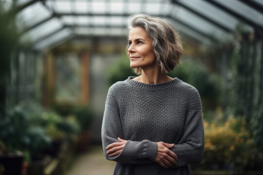 Full-length portrait photography of a satisfied woman in her 40s wearing a cozy sweater against a greenhouse or conservatory background. Generative AI