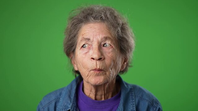 Closeup slow motion portrait of thinking, smart puzzled pensive elderly senior old woman with wrinkled skin looks around thinks has great idea raised finger isolated green screen background