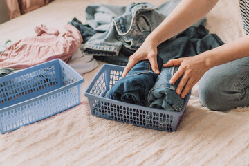 Lady organizes clothes in blue container while sitting on the bed.