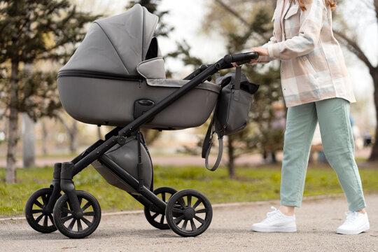 Cropped images of young  pushing stroller with newborn baby inside, walking in spring park. Parenthood, healthy lifestyle concept 