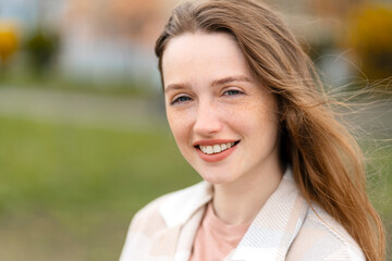 Portrait of beautiful smiling woman with cute freckles on face looking at camera, standing in park. Spring concept 