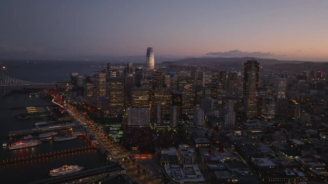 Amazing aerial footage of illuminated downtown skyscrapers on coast against colour twilight sky.