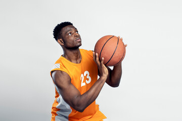 Handsome muscular African man wearing orange sportswear playing basketball, taking shot isolated on white background. Sport competition concept 
