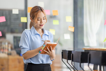 Young business asian woman creative team using post it notes in glass wall to writing finance expert strategy business plan to development grow to success.