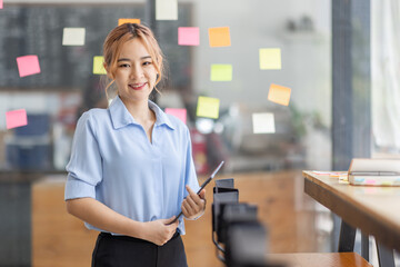 Young business asian woman creative team using post it notes in glass wall to writing finance expert strategy business plan to development grow to success.