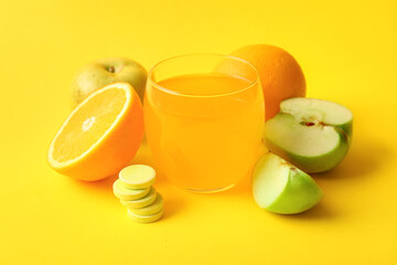 Glass of vitamin C effervescent tablet dissolved in water and fruits on yellow background