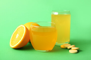 Glasses of vitamin C effervescent tablet dissolved in water and fruits on green background