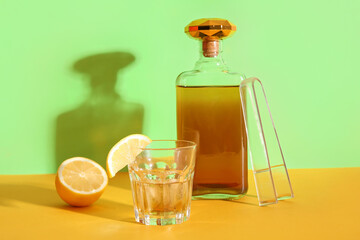 Bottle and glass of cold rum with lemon slice on colorful background
