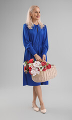 Mature woman with basket of flowers on grey background