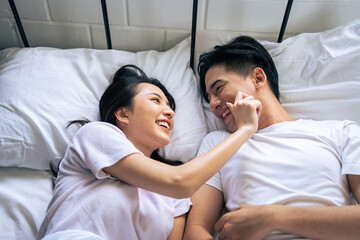 Fototapeta na wymiar Asian new marriage couple lying down on bed and looking at each other. 