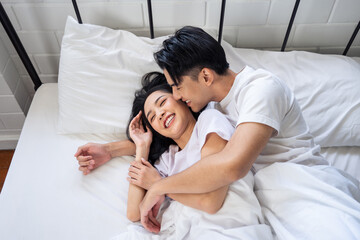 Asian husband kissing his wife while lying down sleep on bed in bedroom. 