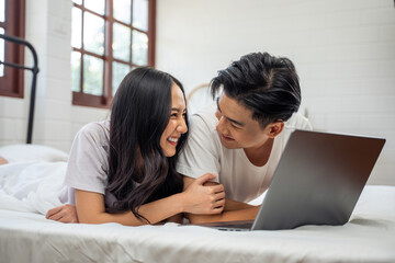 Asian attractive woman using laptop on bed with husband in the morning. 
