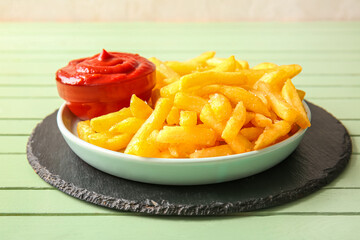 Plate with tasty french fries and bowl of ketchup on color wooden background