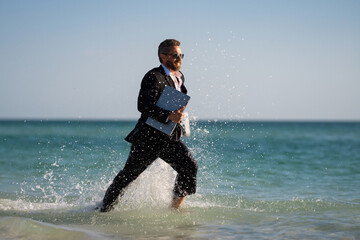 Leisure weekend and remote freelance work. Crazy comic business man in suit run on sea. Funny businessman with laptop runnig on water. Remote summer business. Summer travel holiday for businessman.