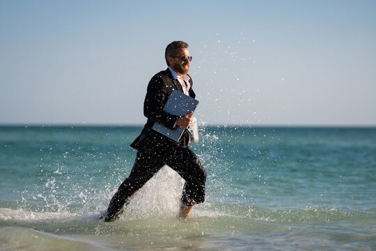 Leisure weekend and remote freelance work. Crazy comic business man in suit run on sea. Funny businessman with laptop runnig on water. Remote summer business. Summer travel holiday for businessman.