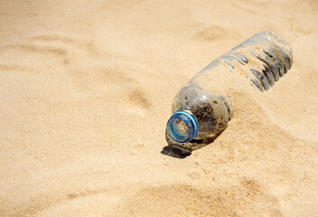 Plastic bottle on sandy beach. Empty uncapped used plastic drinking water bottles piled up with sand, dumped on the beach with copy space. Polluted garbage abandoned by tourists.