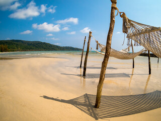 Three empty rope cradle hanging on the wooden poles on sandy beach, island and blue sky background, fisheye view. Beautiful shadow of hanging cradle or swing beds on clean sand beach.