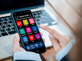 Smart home applications technology on smartphone holding in hand. Smart house app screen on mobile phone for wireless remote connection control using by business person who working with computer.