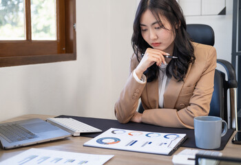Portrait of stressed businesswoman analyzing documents in office. Asian businesswoman sitting at desk reading documents. analyzing graph working on company project. Thoughtful young executives. © Fahng