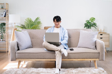 Happy satisfied millennial man using laptop at living room, working from home, reading message with good news, thinking, looking at screen, watching online webinar, training, making payment
