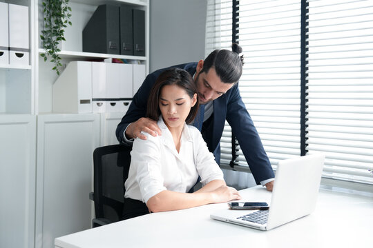 Asian pretty businesswoman sitting and looking at boss flirting by hand touch a shoulder at the workspace in office