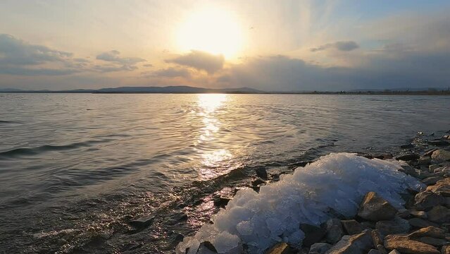 The last unmelted ice on the shore of the lake. Sunset, beautiful clouds in the sky and sun rays.