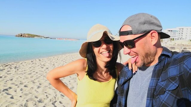 Young caucasian travelers couple enjoy time together on beach vacation pose laugh have good times in summer. Show tongues laugh visit Nissi beach holidays destination in Cyprus.
