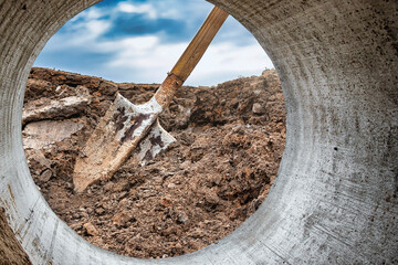 Dirty shovel in fresh soil at a construction site in a pit. Deep hole in the ground. Earthworks,...