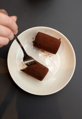White plate with chocolate dessert and woman hand with a fork on black table