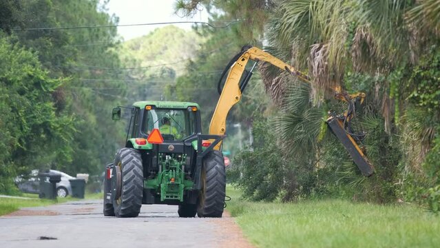 Public works utility tractor pruning trees and greenery braches on Florida rural street side
