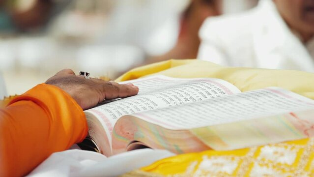 Priest's hand turns page of sacred religious Indian book during wedding ceremony