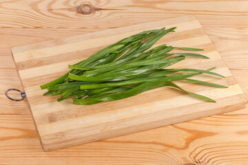 Green stems of garlic on cutting board on rustic table