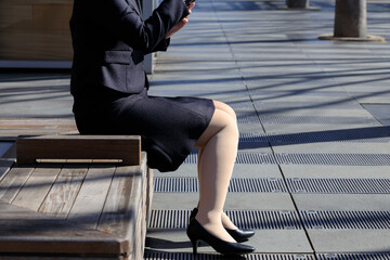 ベンチに座ってスマホを操作している女性　屋外　ビジネス