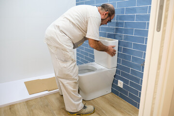 Senior plumber installer installing toilet cistern in a bathroom.