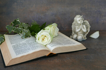 Religiöses Stillleben mit Bibel, Engel, weißen Rosen und Platz für Text.