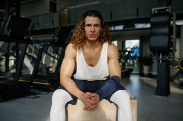 Fototapeta na wymiar Portrait of tired sportsman sitting on fitness box while rest after training