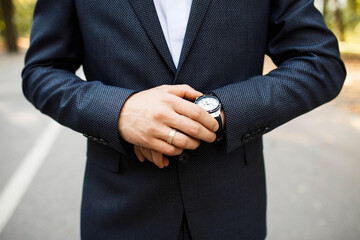 successful married businessman in a dark gray suit pays attention to the watch on his hand. The man pays attention to the time while standing on the road. Close-up