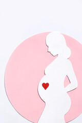 Paper silhouette of a pregnant woman in a pink circle on a white background. Vertical image, flat lay, copy space.