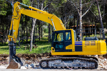 Yellow excavator working on the construction site on the forest road